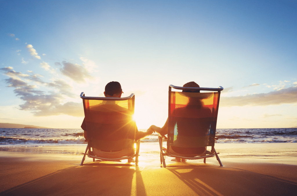 Two people sit in chairs on a beach holding hands