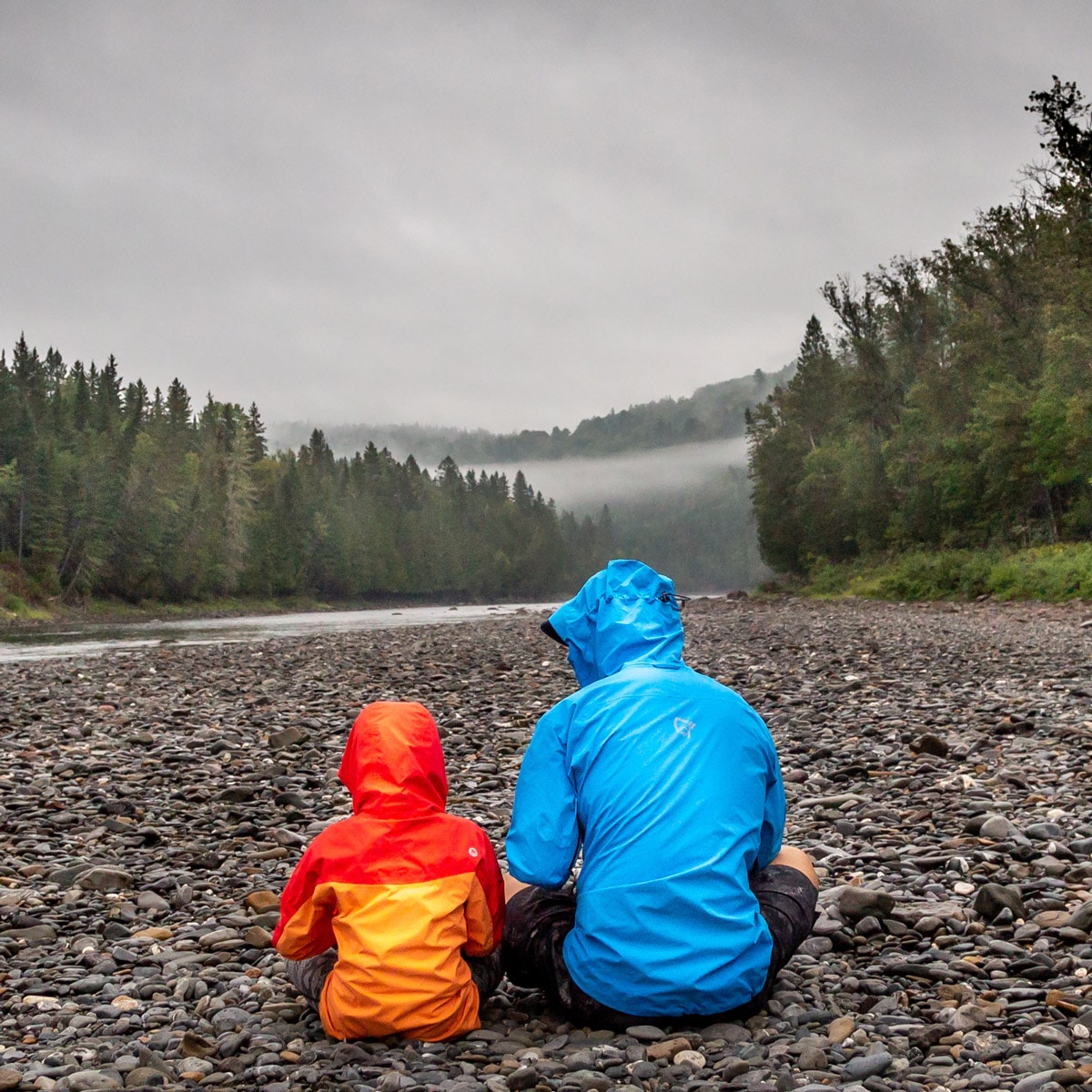 Dad and son sitting by river in forest