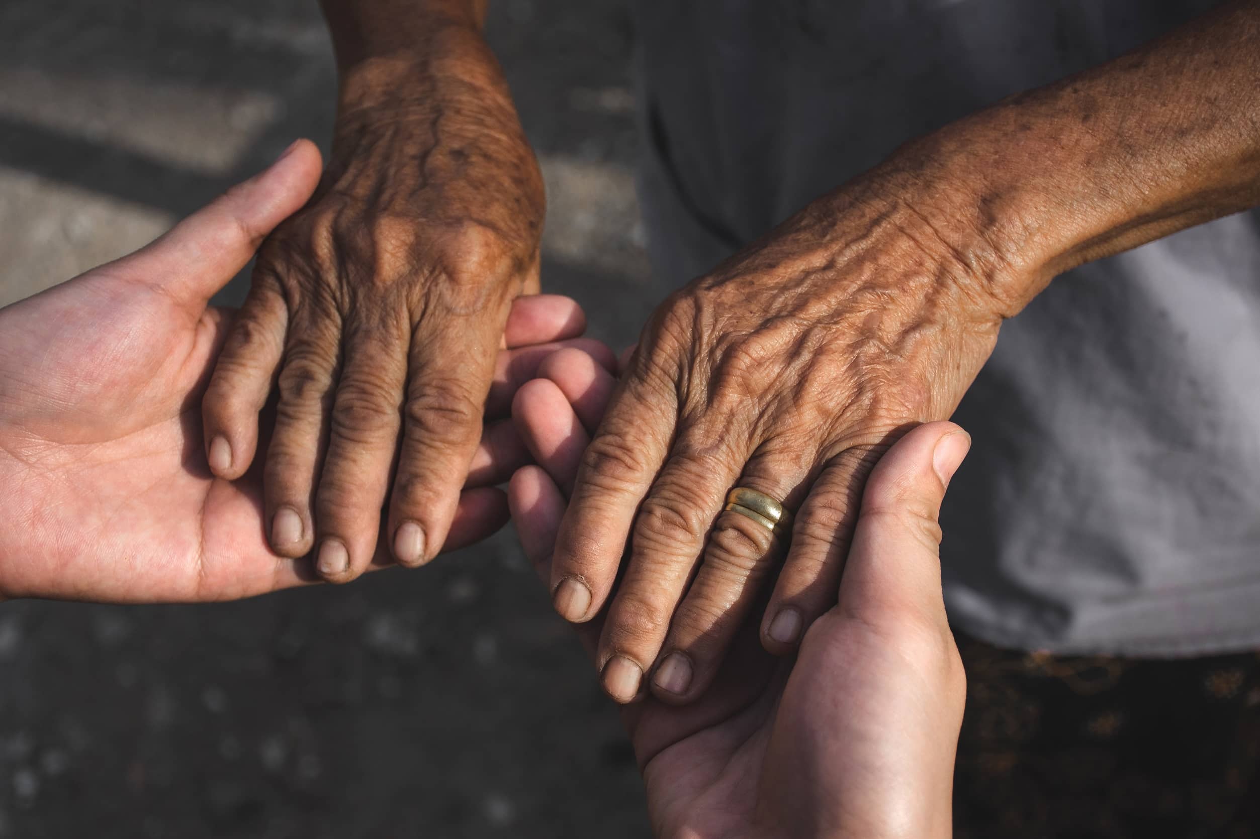 Picture of two young woman hands holding elderly person's hands.